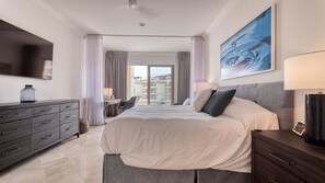 Quarto de hotel com uma cama grande, uma escrivaninha com cadeira, penteadeira, televisão e varanda com cortinas.