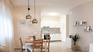 A modern living room with a dining area, kitchen, and a small balcony with a plant.