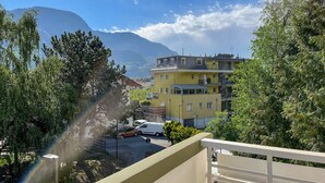 A yellow multi-story building with balconies, surrounded by trees and mountains in the background.