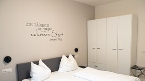 A bedroom with a bed, pillows, a wardrobe, and a wall with a motivational quote.