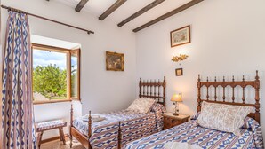 Un dormitorio con dos camas, una ventana con vistas a zonas verdes, un cabecero de madera y una mesita de noche con lámpara.