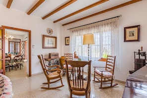 Une pièce meublée de meubles en bois, avec une table à manger, des chaises, une lampe et une fenêtre ornée de rideaux en dentelle.