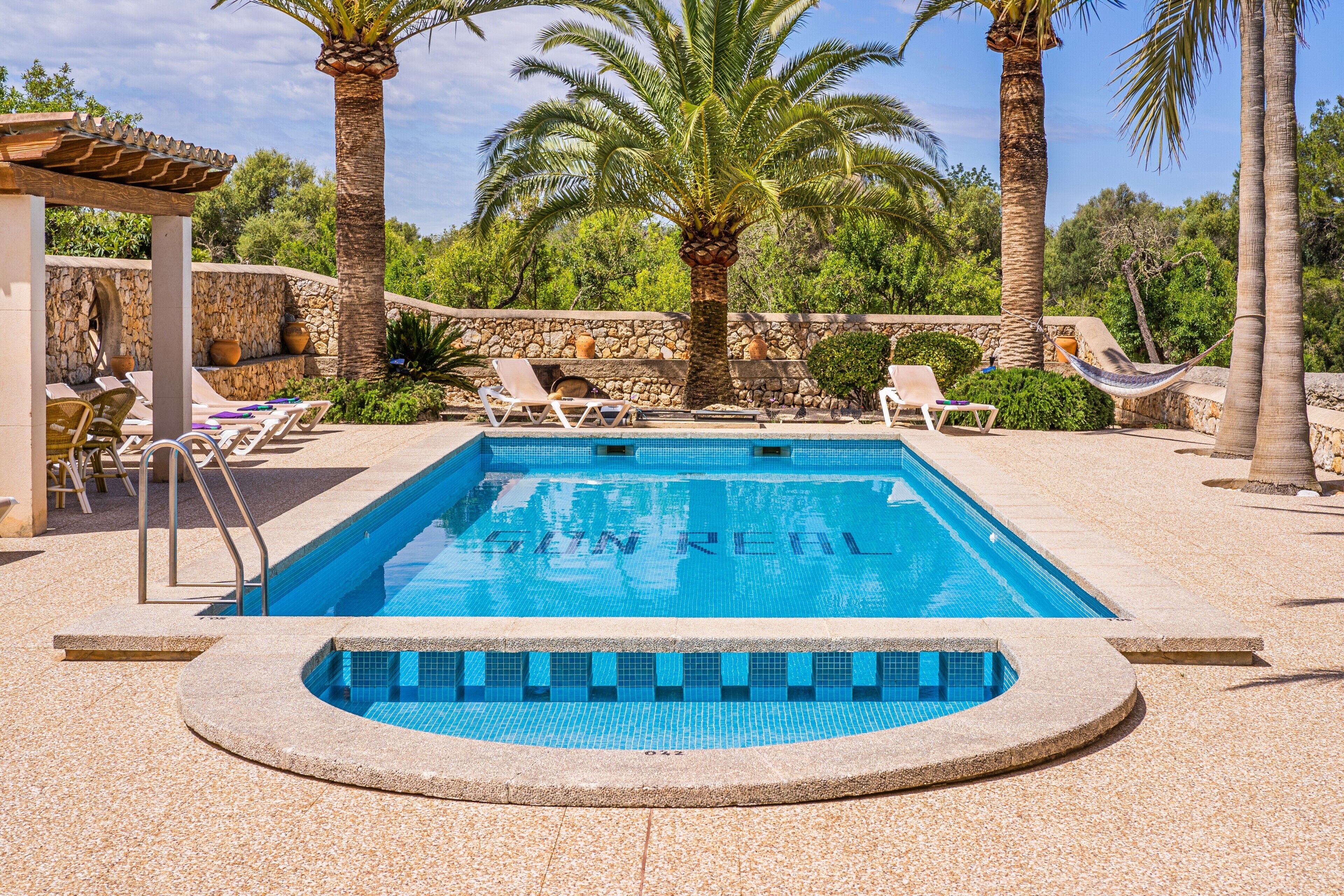 Une piscine rectangulaire bordée de pierres, entourée de chaises longues et de palmiers.