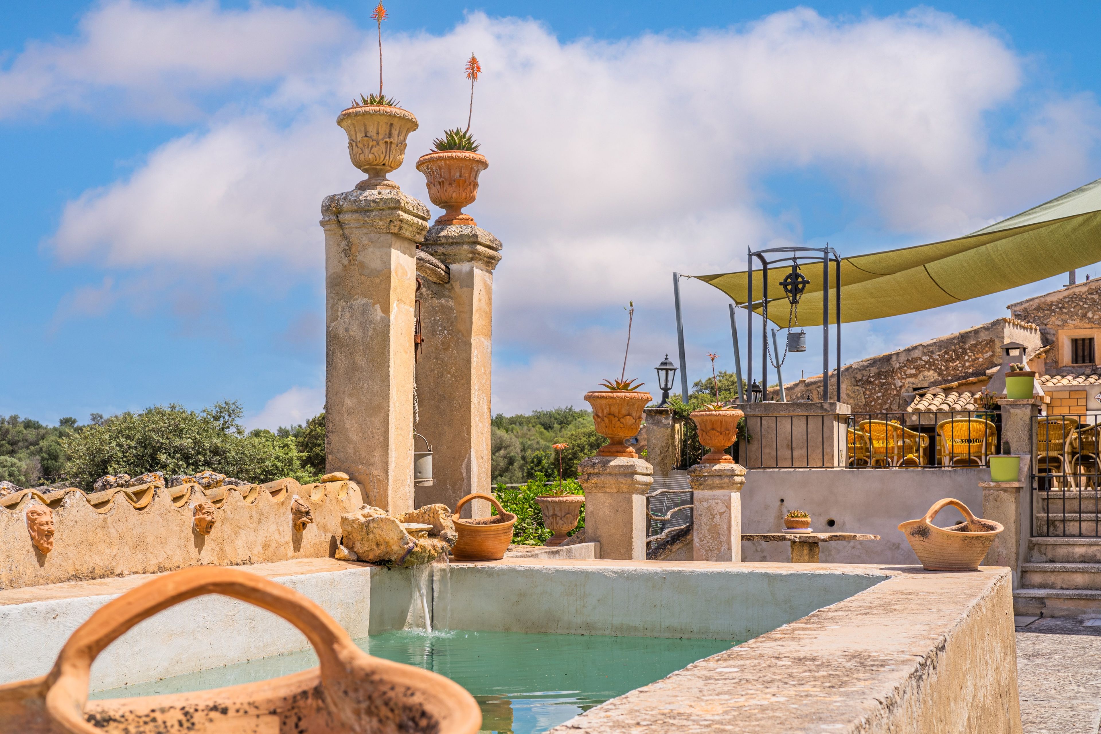 A traditional fountain with multiple urns, a pool, and a shaded area with chairs.