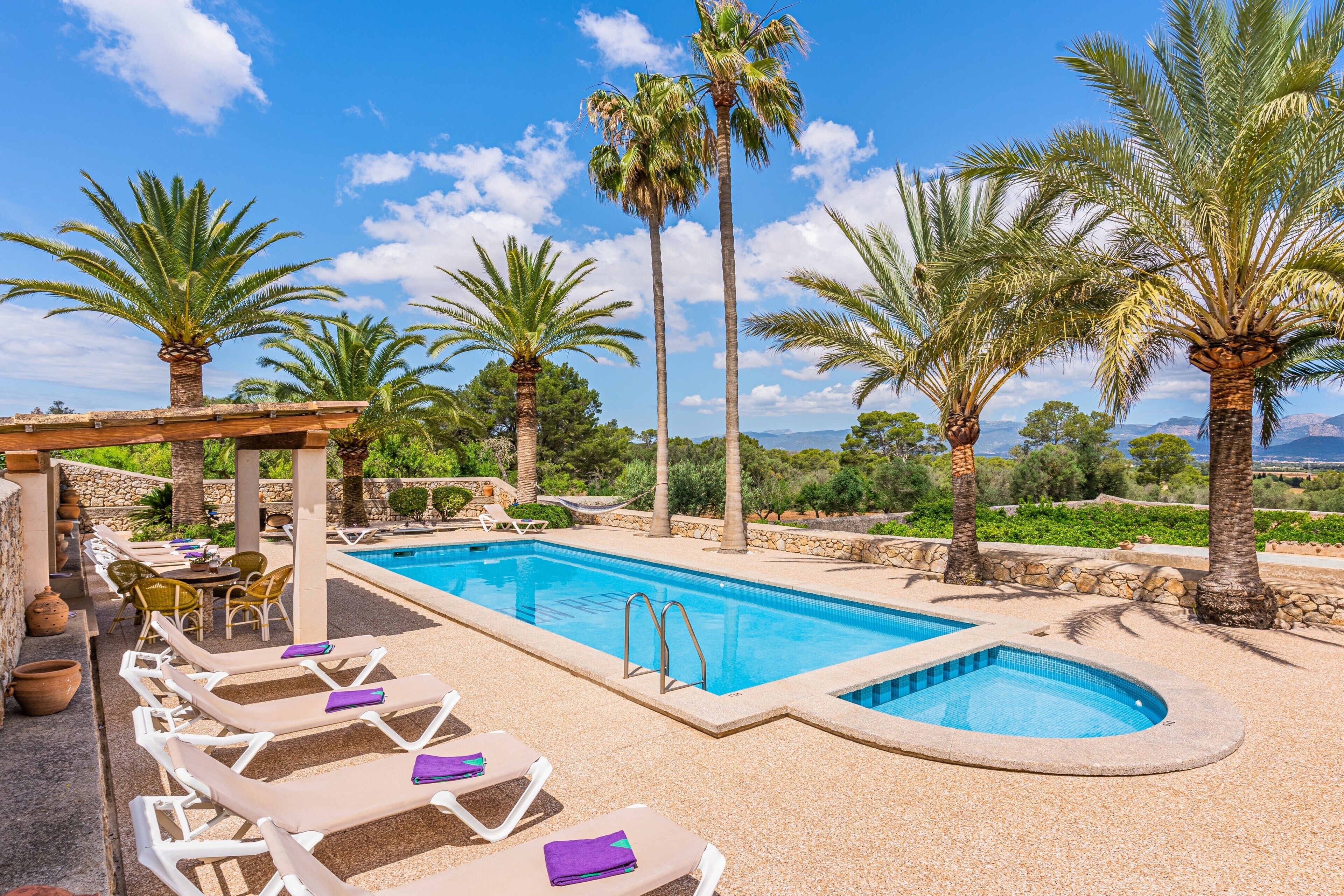A pool area with lounge chairs and a stone wall.