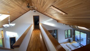 Una habitación con techos altos, vigas de madera, un ventilador de techo y vistas a otra habitación por una puerta.