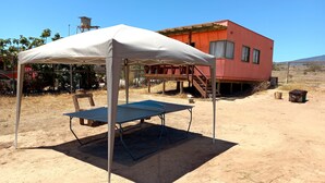 Ein Zelt mit Tisch in einer offenen, trockenen Landschaft, im Hintergrund ein rotes Gebäude.