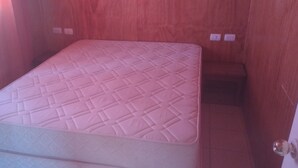 Ein Einzelbett mit gesteppter Matratze in einem Raum mit Holzwänden und einer Tür.