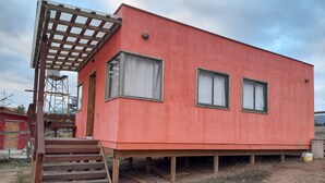 Ein rotes Gebäude mit einer Holztreppe, die zu einer Tür und zwei Fenstern führt, sowie einer Holzpergola.