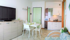 Un espacio habitable compacto con televisión, una mesa de comedor con sillas, una kitchenette y un pequeño sofá.