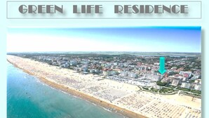 Vista aérea de una ciudad costera con playa, edificios y una residencia ecológica señalada con una flecha verde.