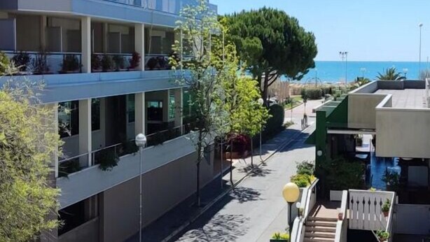 Un hotel de varios pisos con balcones, vistas despejadas al mar y un jardín bien cuidado.