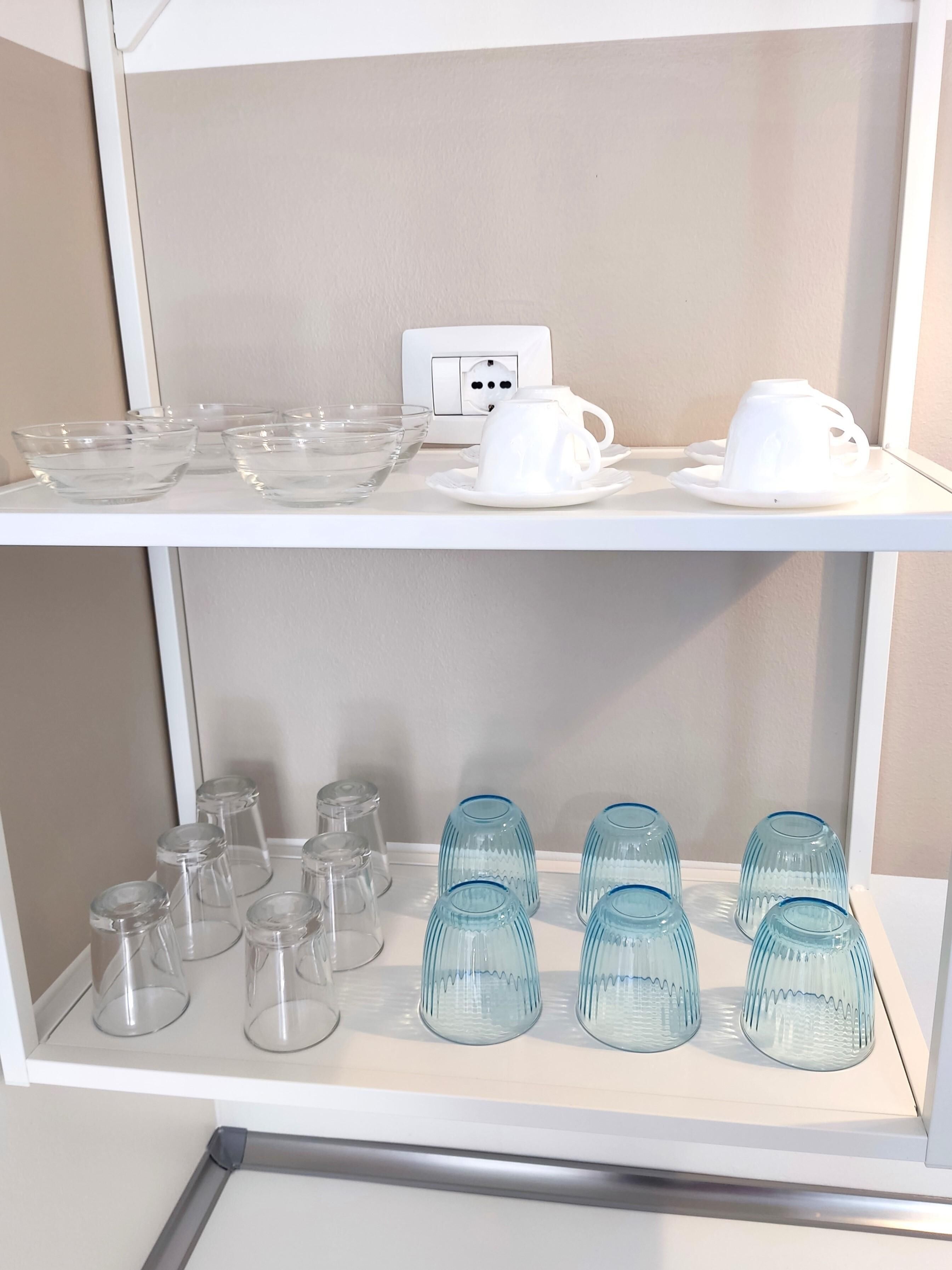 A shelf with clear glass bowls and blue glass cups.