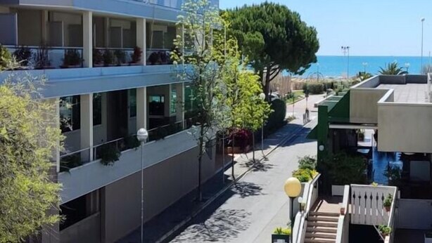 A multi-story hotel with balconies, a street view, and a clear blue sky.
