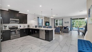 Una cocina moderna con armarios oscuros, una isla central y un área de comedor con un sofá y sillas azules.