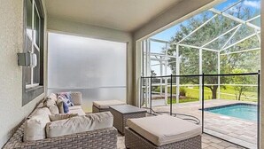 Un patio techado con mobiliario de mimbre, una piscina y vistas al exterior.