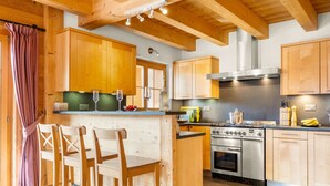 Een moderne keuken met houten kasten, een centraal eiland met barstoelen, roestvrijstalen apparatuur en een groot raam.