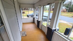 A covered porch with a wooden floor, white siding, and large windows.