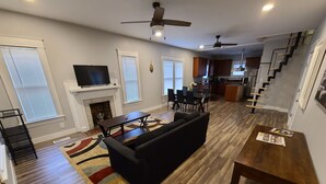 A modern living room with a fireplace, black sofa, dining table, and kitchen area in the background.