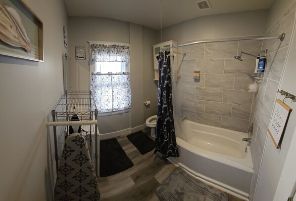 A bathroom with a bathtub, shower, toilet, and a window with curtains.