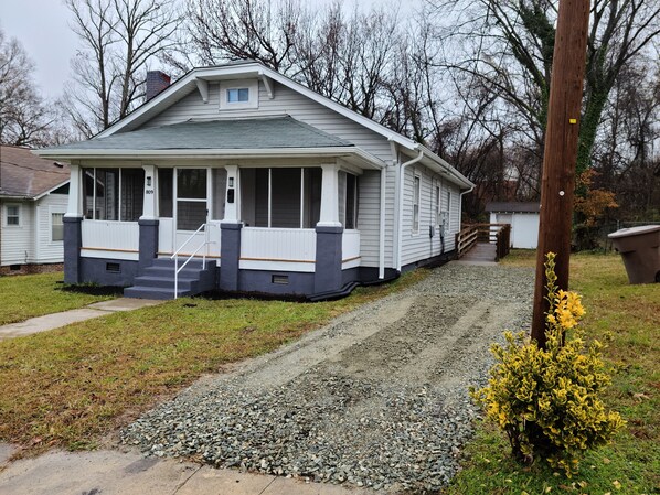 A single-story house with a front porch, a small attached garage, and a gravel driveway. - Next to Downtown Greensboro 3 Bedroom / 2 Bathroom Bungalow (Greensboro)