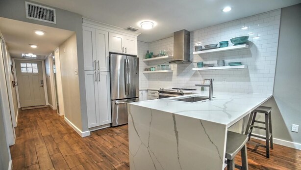 A modern kitchen with white cabinetry, a marble island, and wooden flooring.