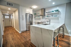 A modern kitchen with white cabinetry, a marble island, and wooden flooring.