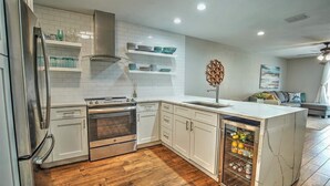 A modern kitchen with white cabinets, a stainless steel refrigerator, a built-in oven, and a marble island with a wine cooler.