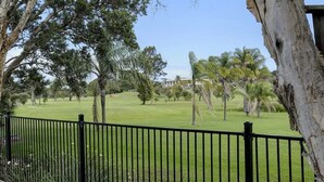 A grassy area with a black metal fence, trees, and a building in the background. - Retreat on Gleeson (Forster)