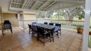 A covered patio with a wooden table and chairs, a bench, and a potted plant. - Retreat on Gleeson (Forster)