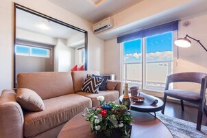 A modern living room with a brown sofa, a round coffee table with a floral centerpiece, a chair, and a large window with a view of the sky.