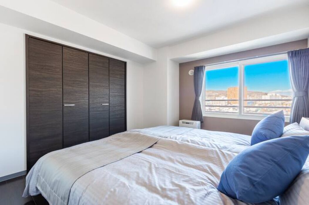Un dormitorio con una cama grande, un armario y una ventana con vista a la ciudad.