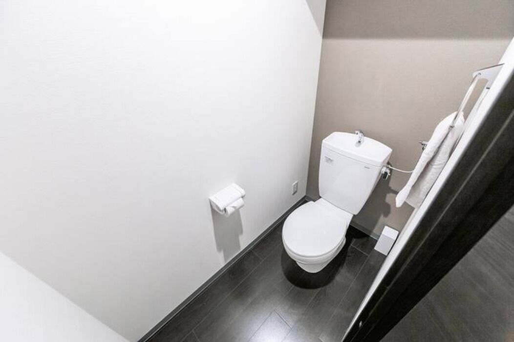 Ein kleines, modernes Badezimmer mit Toilette, Handtuchhalter und dunklem Boden.