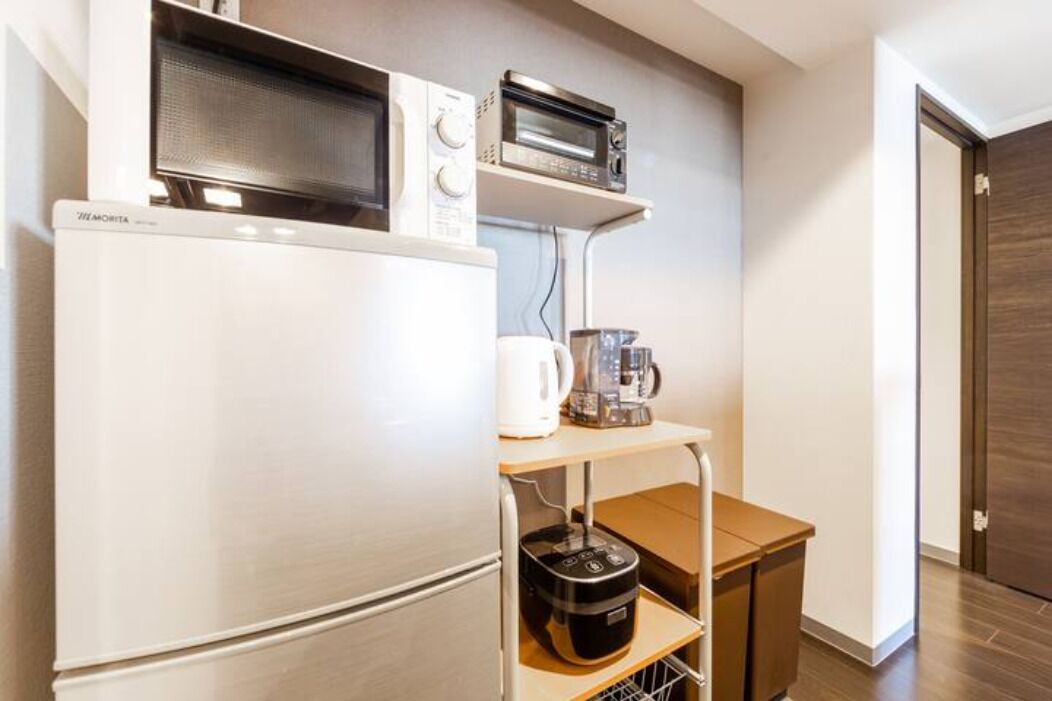 A compact kitchenette with a refrigerator, microwave, toaster, and coffee maker on a shelf.