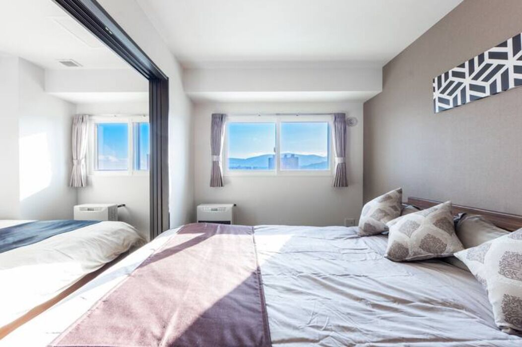 Una habitación de hotel moderna con dos camas, un ventanal con vistas a la ciudad y una decoración geométrica en la pared.