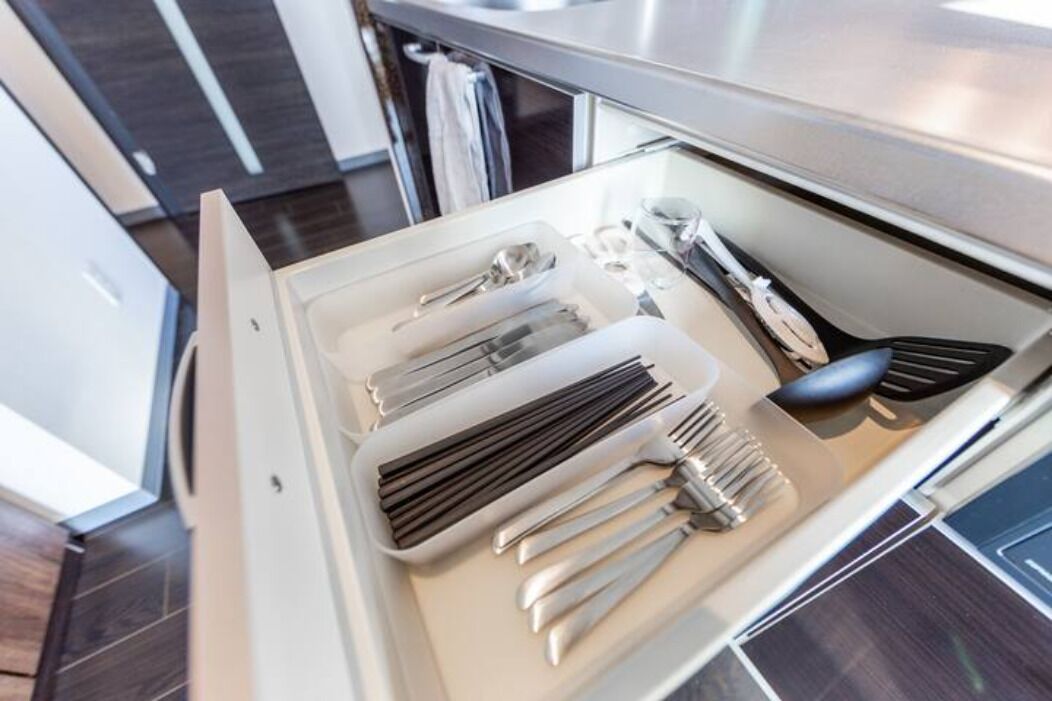 A kitchen drawer with utensils neatly organized, including knives, a spatula, and a whisk.