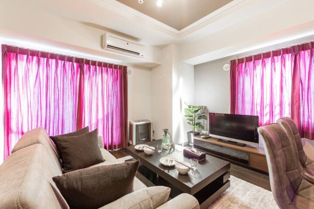 Una sala de estar con un sofá, una mesa de centro, un televisor y cortinas rosas.