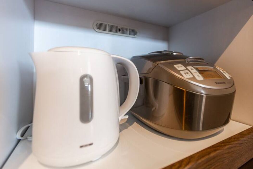 A white electric kettle and a stainless steel coffee maker on a white countertop.