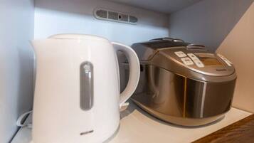 A white electric kettle and a stainless steel coffee maker on a white countertop.
