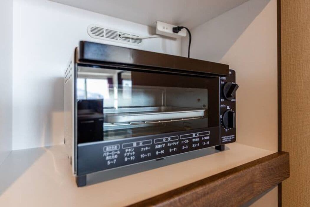 A black toaster oven with a digital display and control panel, placed on a wooden shelf.