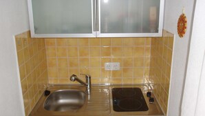 A compact kitchen with a stainless steel sink, a stove, and a white cabinet above. - HAUS Toscana - 350 m to the beach, terrace/garden - Holiday home Toscana (Koserow)