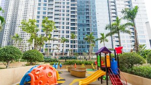 A playground with slides and climbing structures, surrounded by palm trees and modern buildings. - Hoasun Skyview Sunwah Pearl (Ho Chi Minh City)