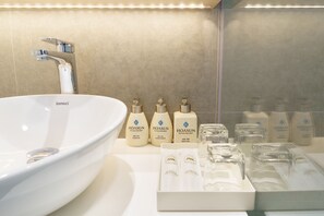 Une salle de bain avec un lavabo blanc, plusieurs bouteilles de shampoing et d’après-shampoing de la marque Hoasun, et des articles de toilette rangés avec soin.
