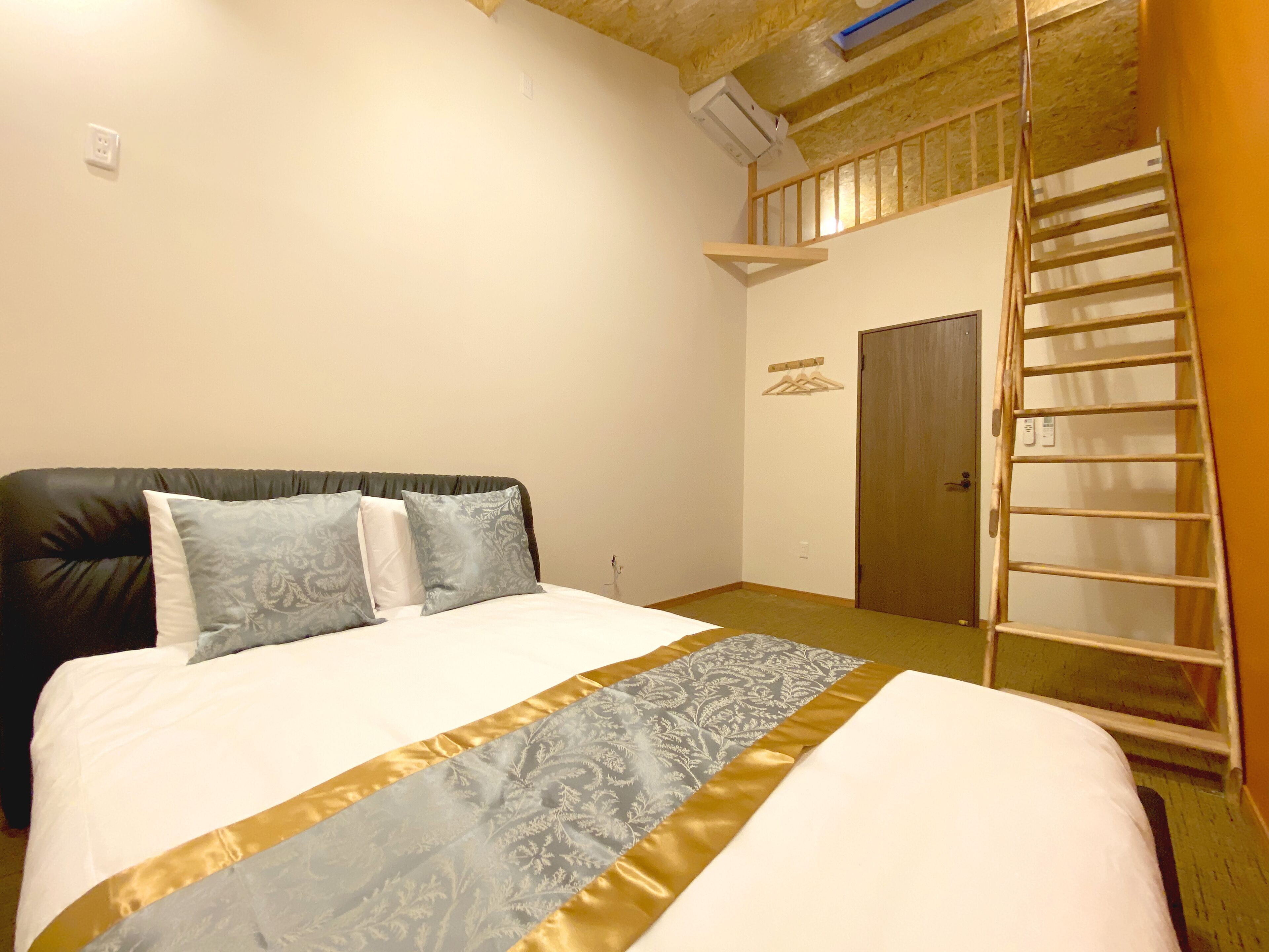 A bedroom with a bed, a wooden ladder, a door, and a wall-mounted shelf.