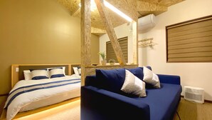A bedroom with a bed, a blue sofa, a mirror, and a window with blinds. - Diamond YU (Fujikawaguchiko)