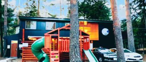 A playground with a slide, climbing area, and a small building with a window.