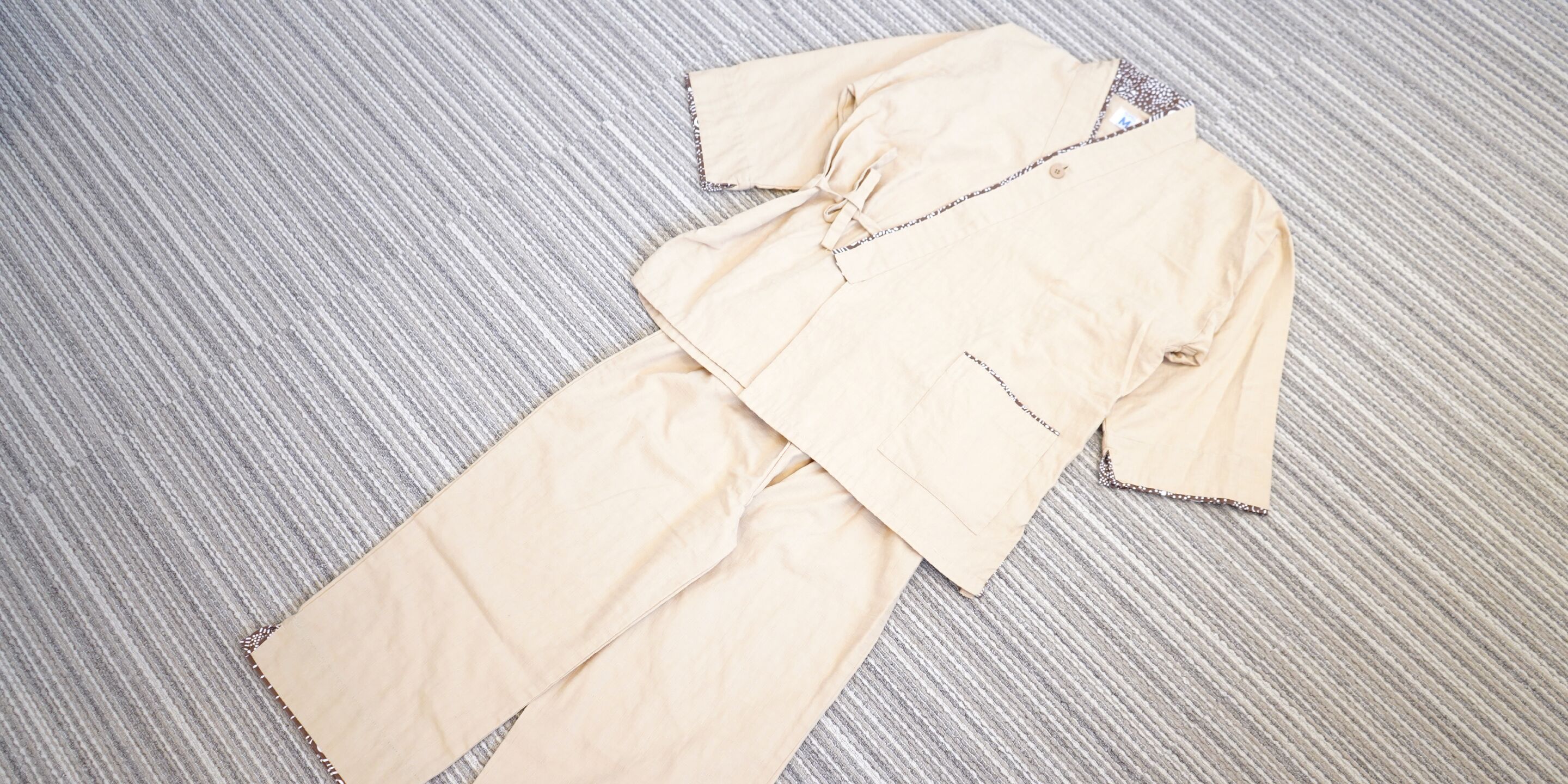 A beige outfit laid out on a striped carpet.