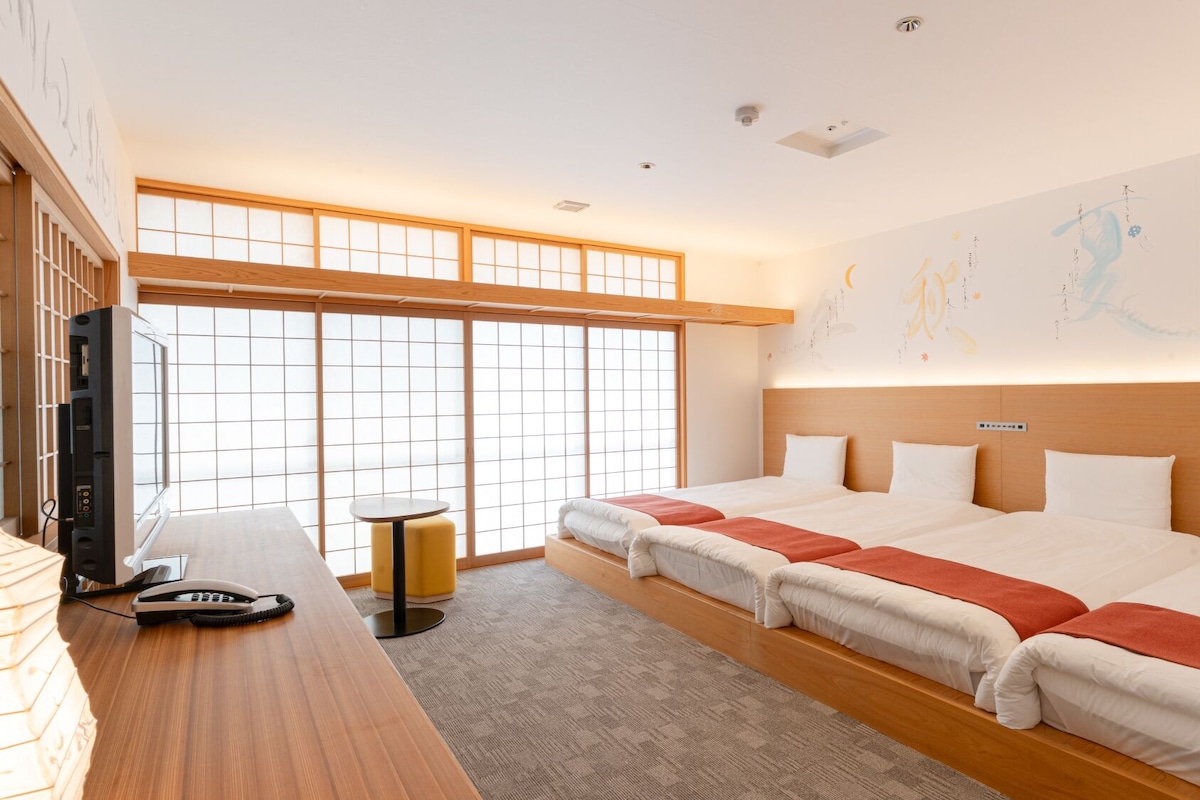 Una habitación de hotel con un ventanal grande, un escritorio con teléfono y una cama con una colcha roja.