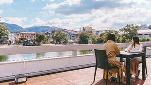 Two people sitting at a table with a view of a river and buildings in the background. - Hotel Tenpyo Naramachi (Nara)