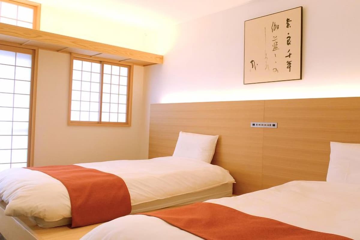 Habitación de hotel con dos camas, cabecero de madera, ventana con diseño de cuadrícula y una obra de arte colgada en la pared.